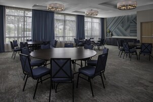 A conference room with a large round table surrounded by chairs, large windows with curtains, and a modern ceiling design.