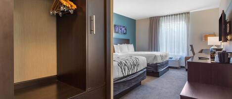 A hotel room with a wardrobe, two beds, a desk, and a window with curtains.