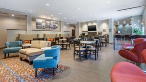 Een moderne hotel lobby met zithoeken, een bar en een televisiescherm.