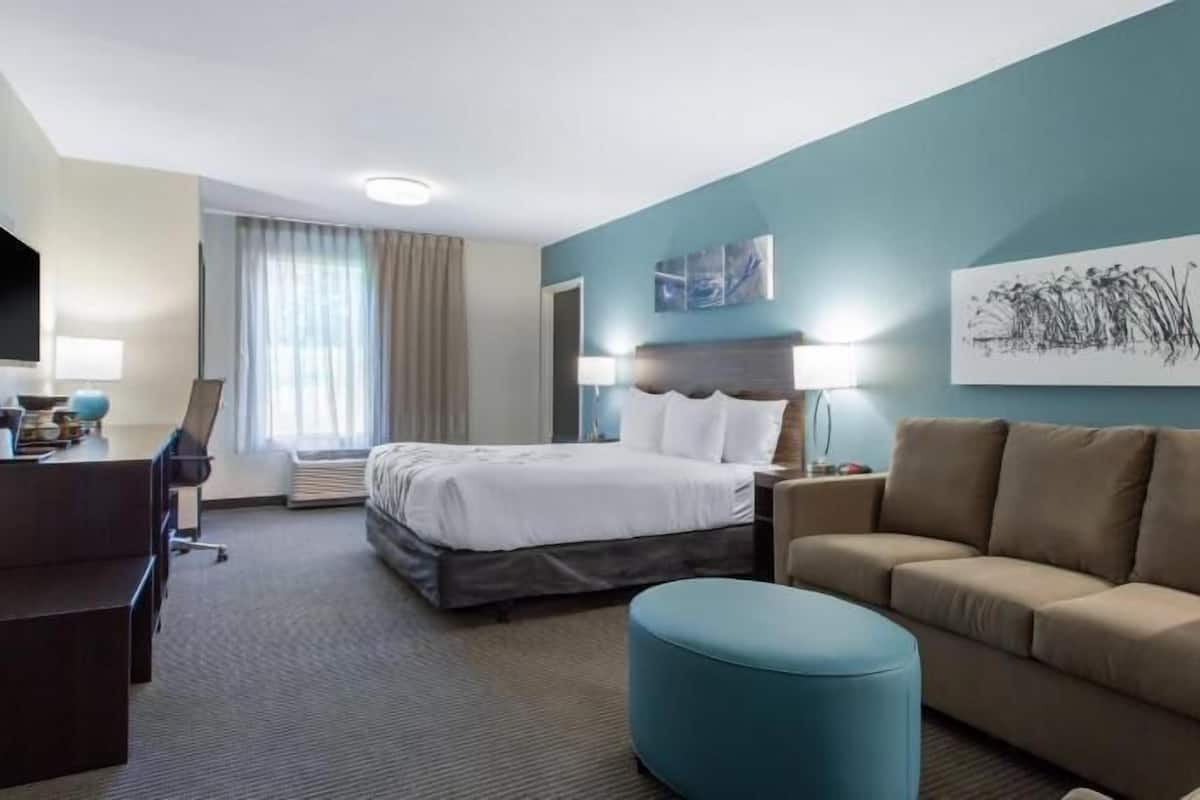 A hotel room with a bed, a desk, a sofa, and a blue ottoman.