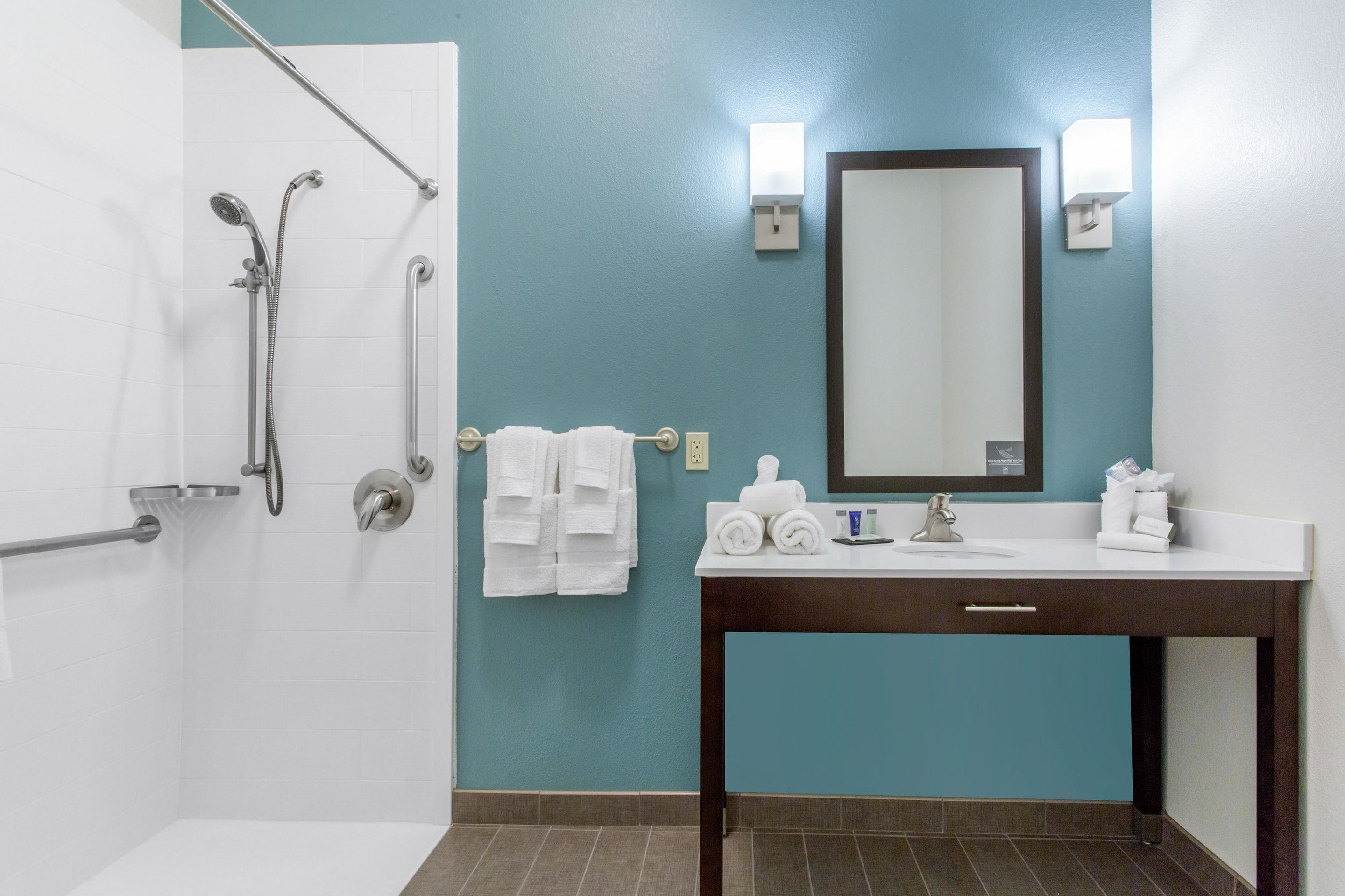 A bathroom with a shower, a sink with a mirror, and towels on a rack.