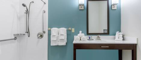 A bathroom with a shower, a sink with a mirror, and towels on a rack.