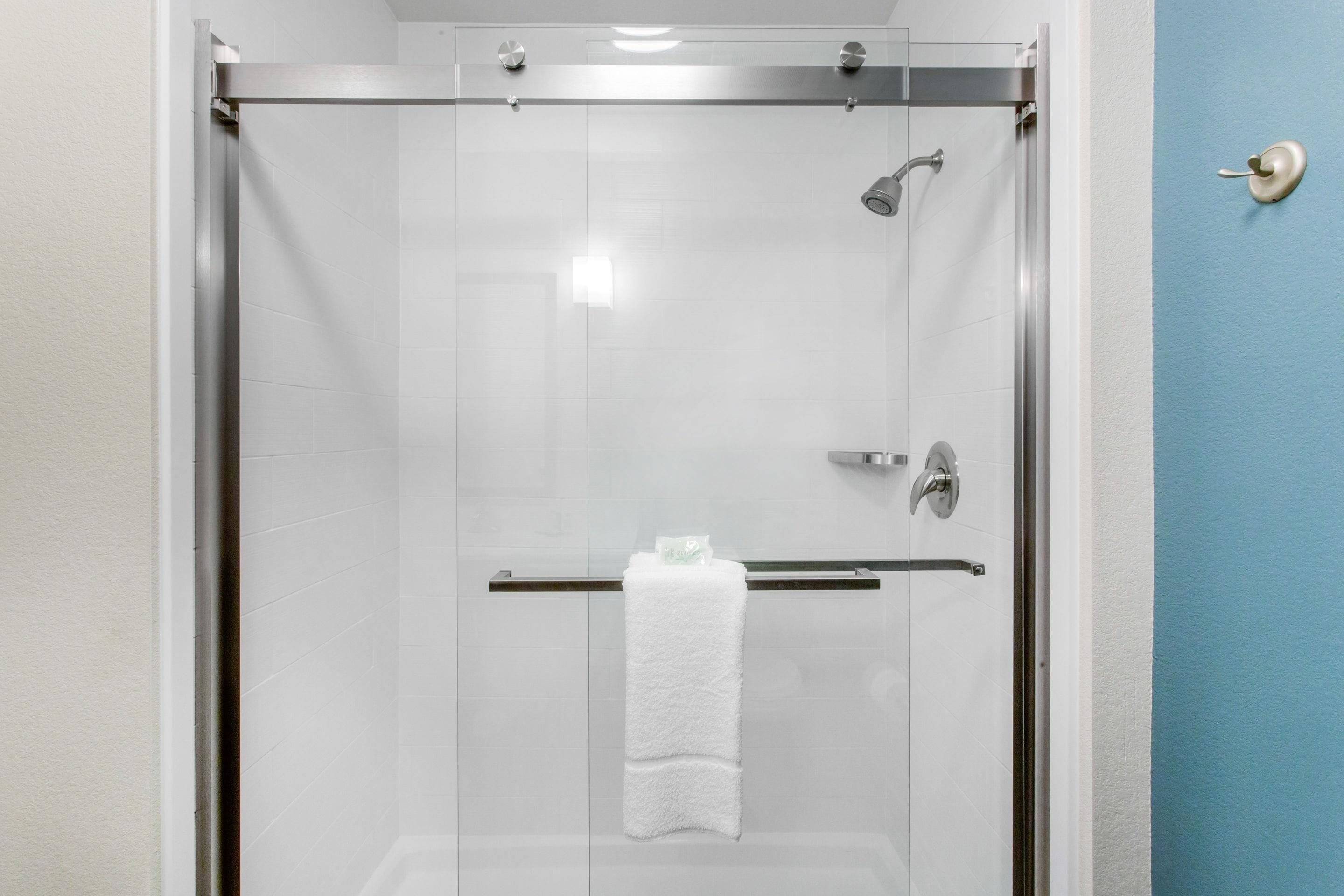 Douche met glazen wand, een witte handdoek hangend aan een metalen stang, een handdouche en een kraan op de muur.