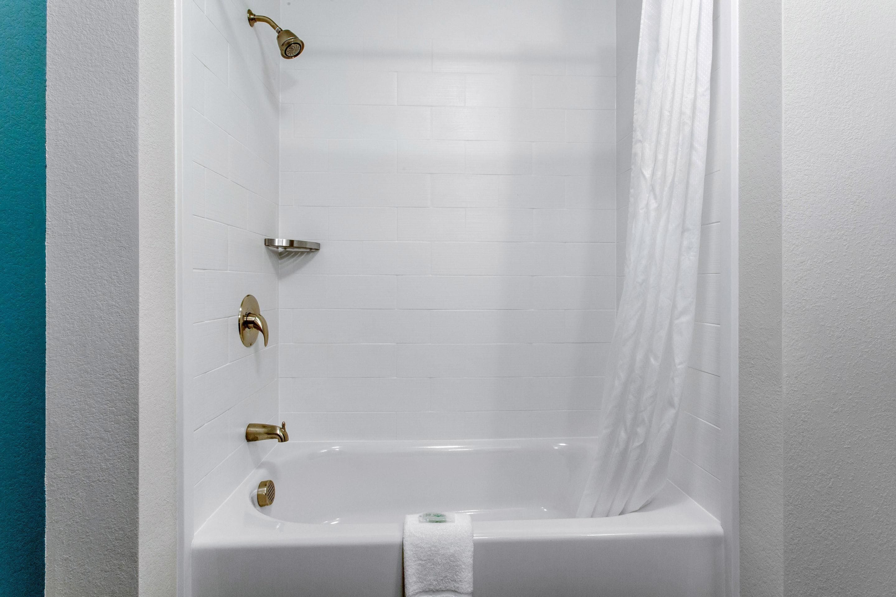 Una bañera blanca con detalles dorados, una toalla blanca y una cortina de ducha.