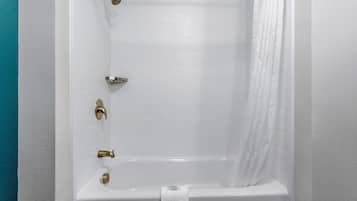 A white bathtub with gold fixtures, a white towel, and a shower curtain.