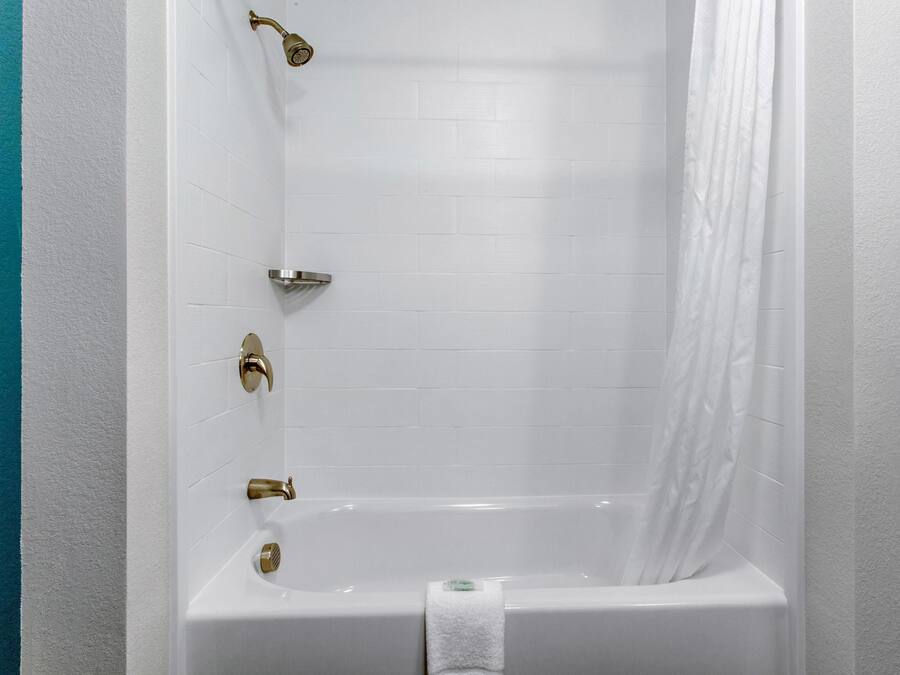 A white bathtub with gold fixtures, a white towel, and a shower curtain.