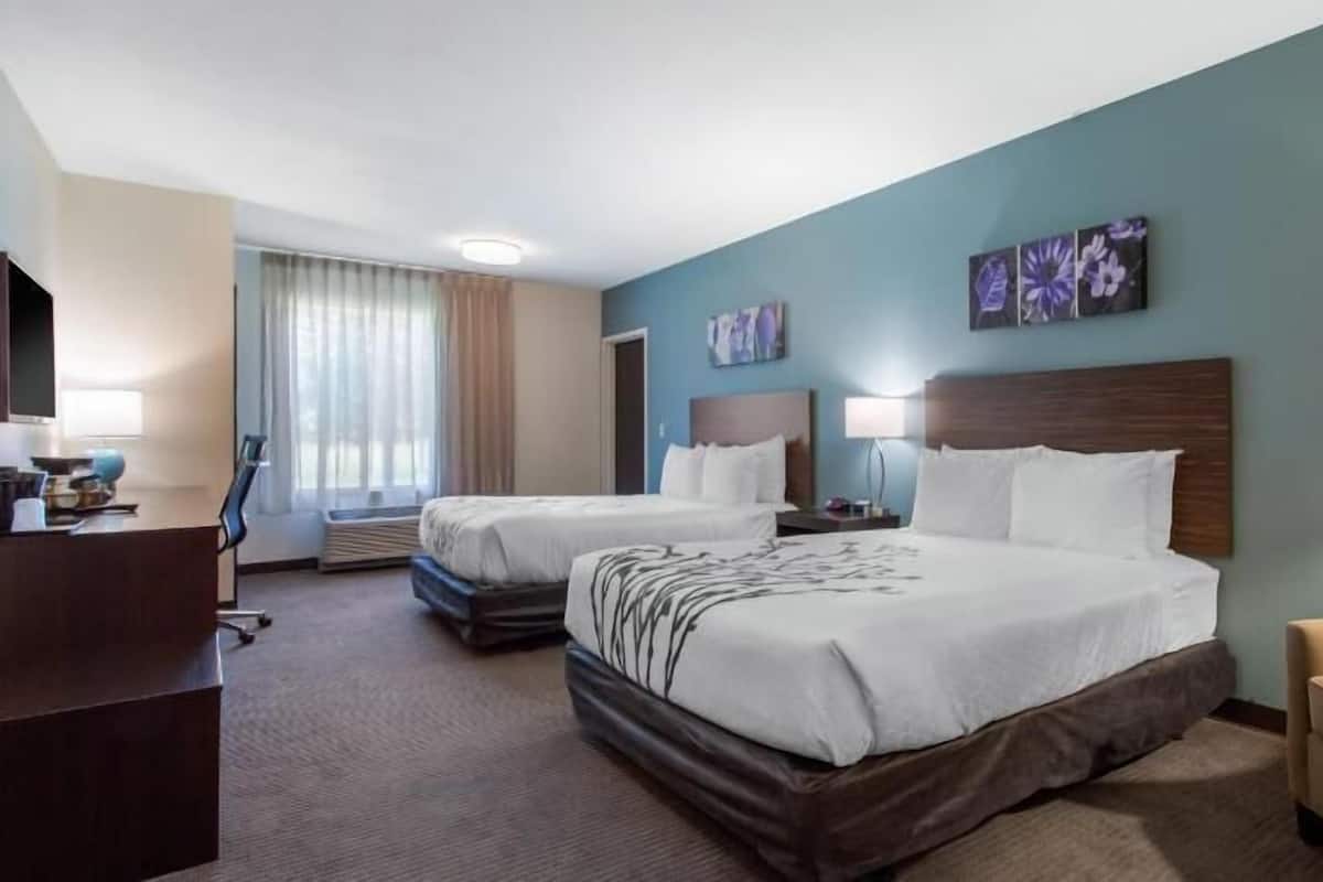 A hotel room with two beds, a desk, a chair, and artwork on the walls.