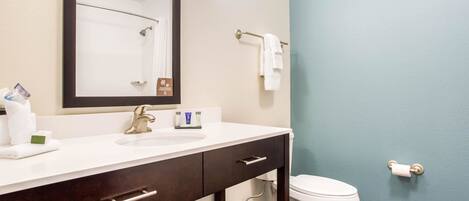 A bathroom with a white sink, dark wooden vanity, a large mirror, a towel rack, and a toilet.