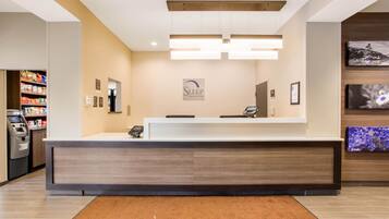 A hotel reception area with a reception desk, a cash register, and a 'Welcome' mat.