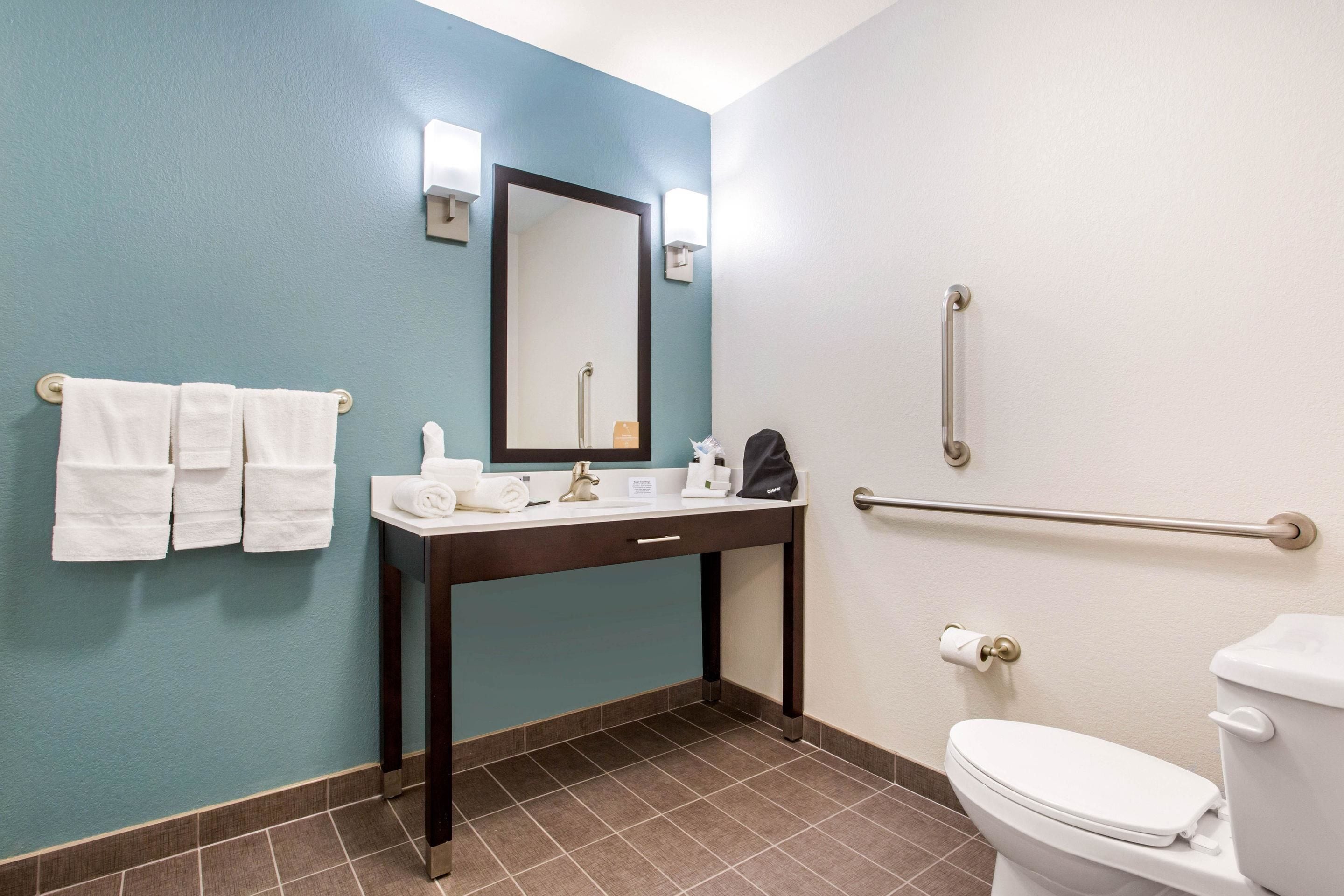 A bathroom with a sink, mirror, towel rack, toilet, and grab bars.
