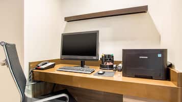 A hotel office with a desk, computer, printer, phone, and chair.