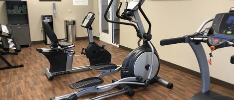 Centro de fitness com máquinas de cardio, televisão e relógio na parede.