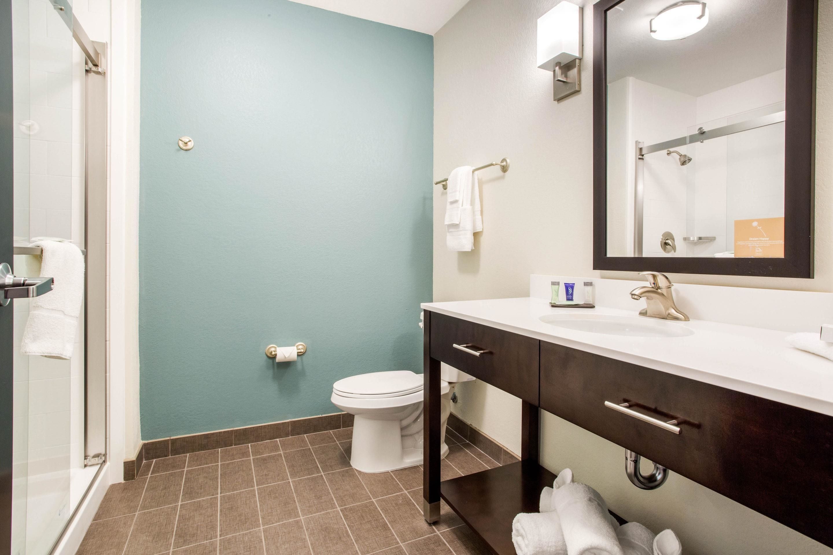 A bathroom with a teal wall, a white toilet, a dark wooden vanity, and a mirror above the sink.