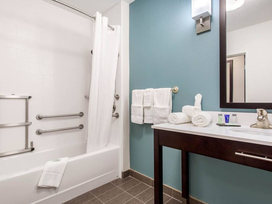 Un baño con bañera, lavamanos, espejo y toallero.
