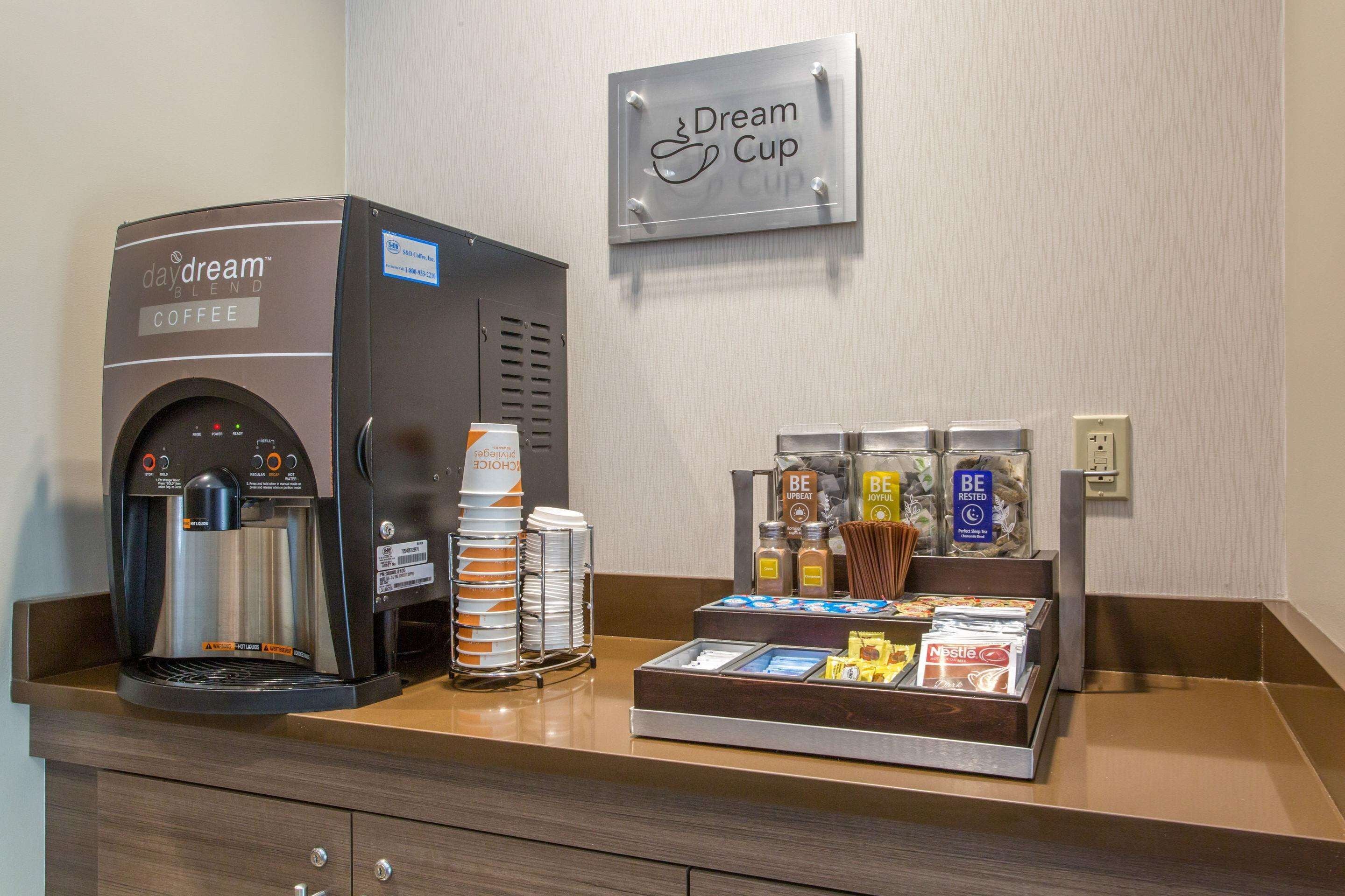 Un espace dédié au café, comprenant une machine à café, des gobelets jetables et un assortiment de capsules de café et de crème liquide.