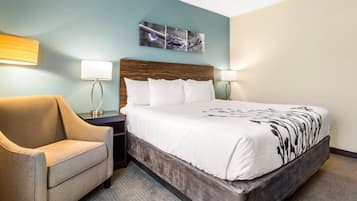 Een hotelkamer met een bed, een stoel, een nachtkastje en een wandlamp.