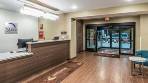 A hotel reception area with a reception desk, a computer, a fire extinguisher, and a glass door entrance. - Sleep Inn & Suites Fort Worth - Fossil Creek (Fort Worth)
