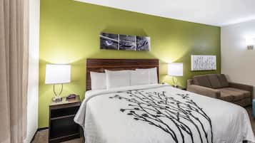 A hotel room with a bed, two bedside lamps, a nightstand, a sofa, and a wall art piece above the bed.