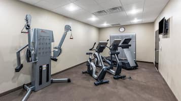 Un gimnasio con bicicletas estáticas, una máquina de poleas y una cinta de correr.