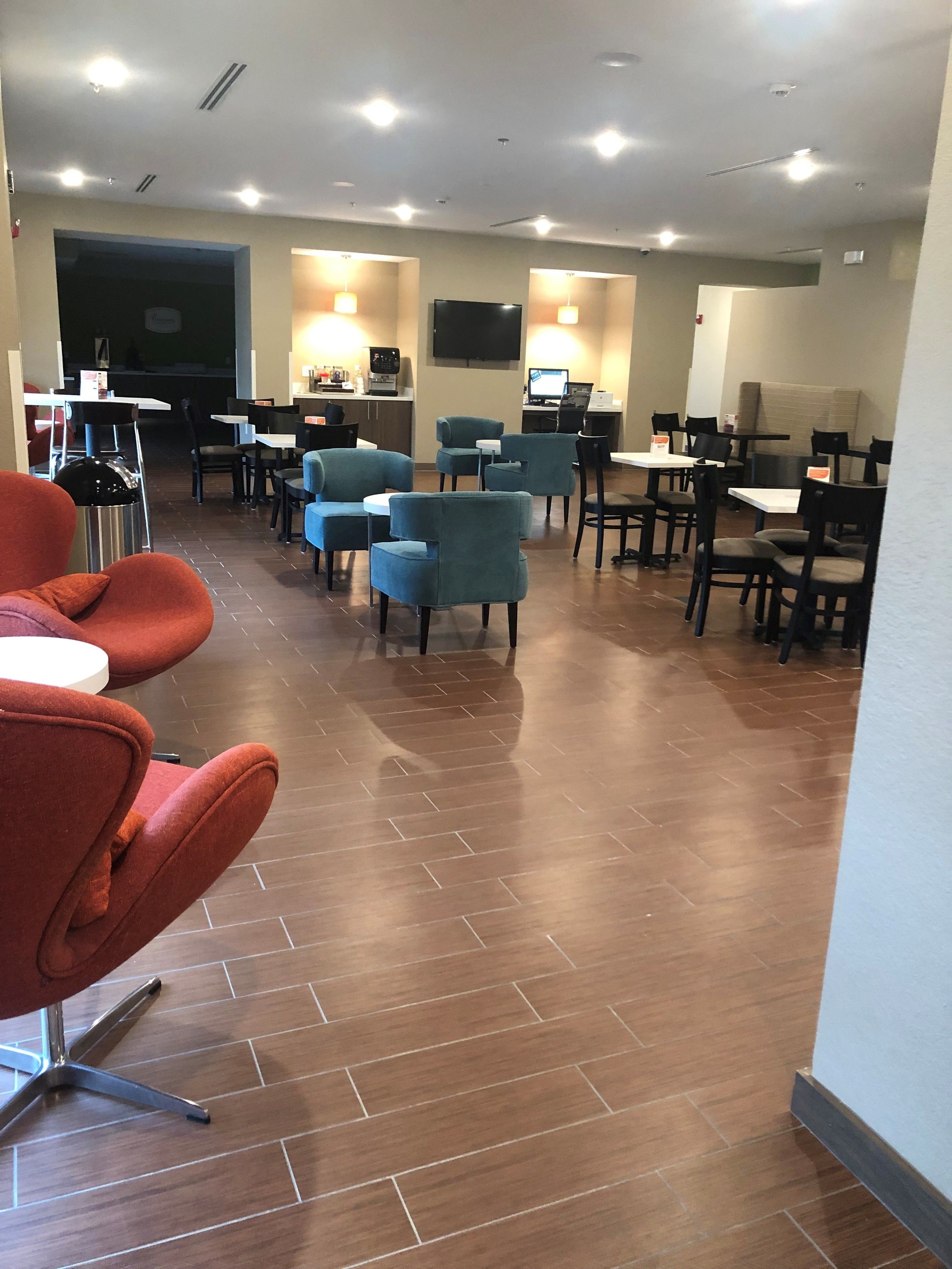 A hotel lobby with multiple seating areas, including red and blue chairs, and a flat-screen TV mounted on the wall.