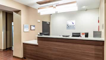 A reception desk with a sign for Sleep Inn & Suites, a check-in/out counter, and a digital screen.