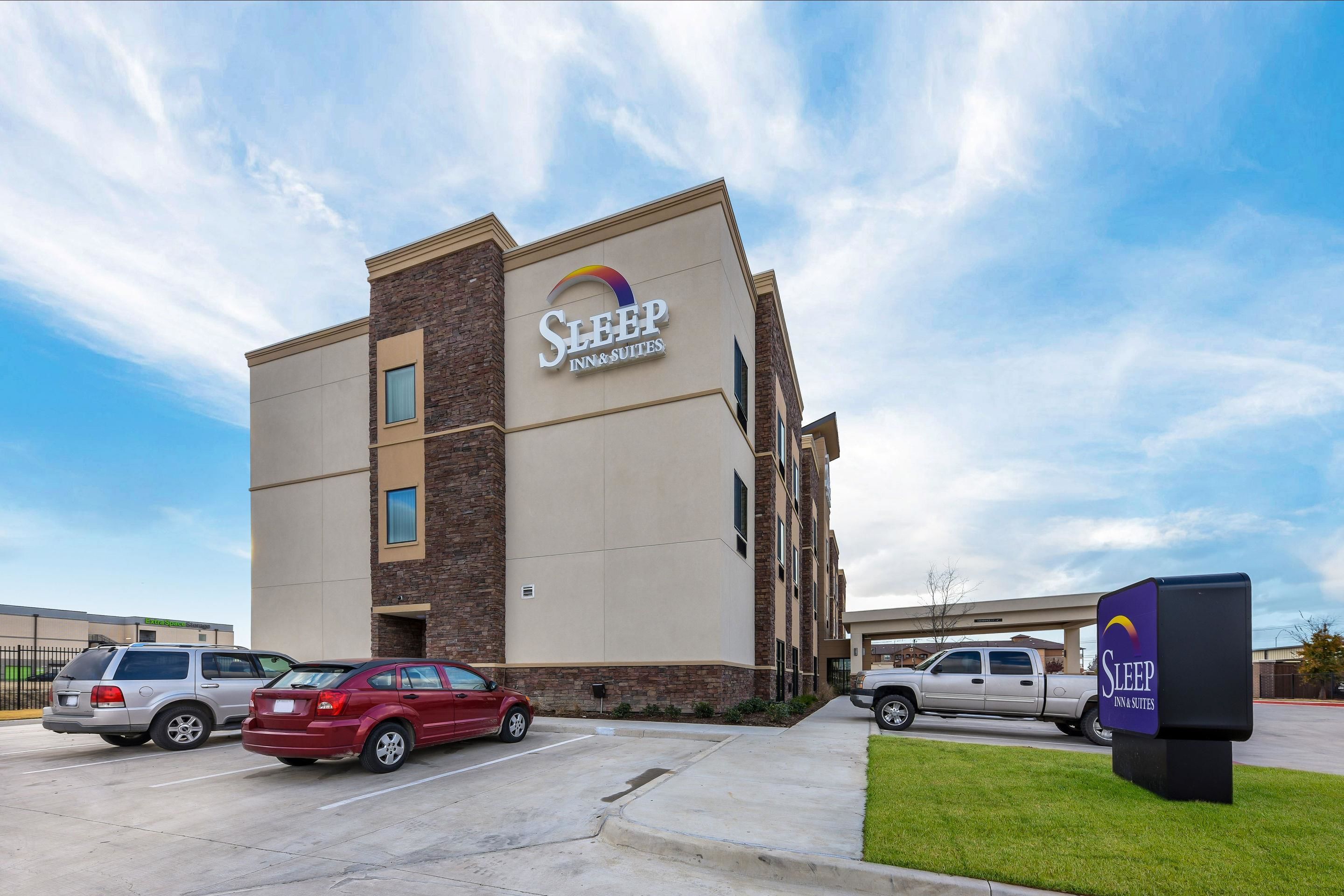 A Sleep Inn & Suites building with a modern design, featuring a prominent sign and a parking lot with several vehicles.