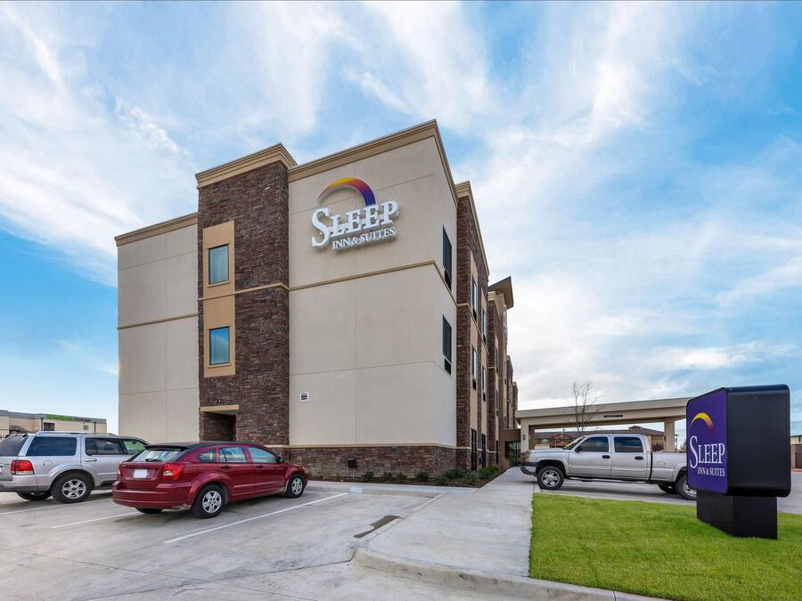 A Sleep Inn & Suites building with a modern design, featuring a prominent sign and a parking lot with several vehicles.