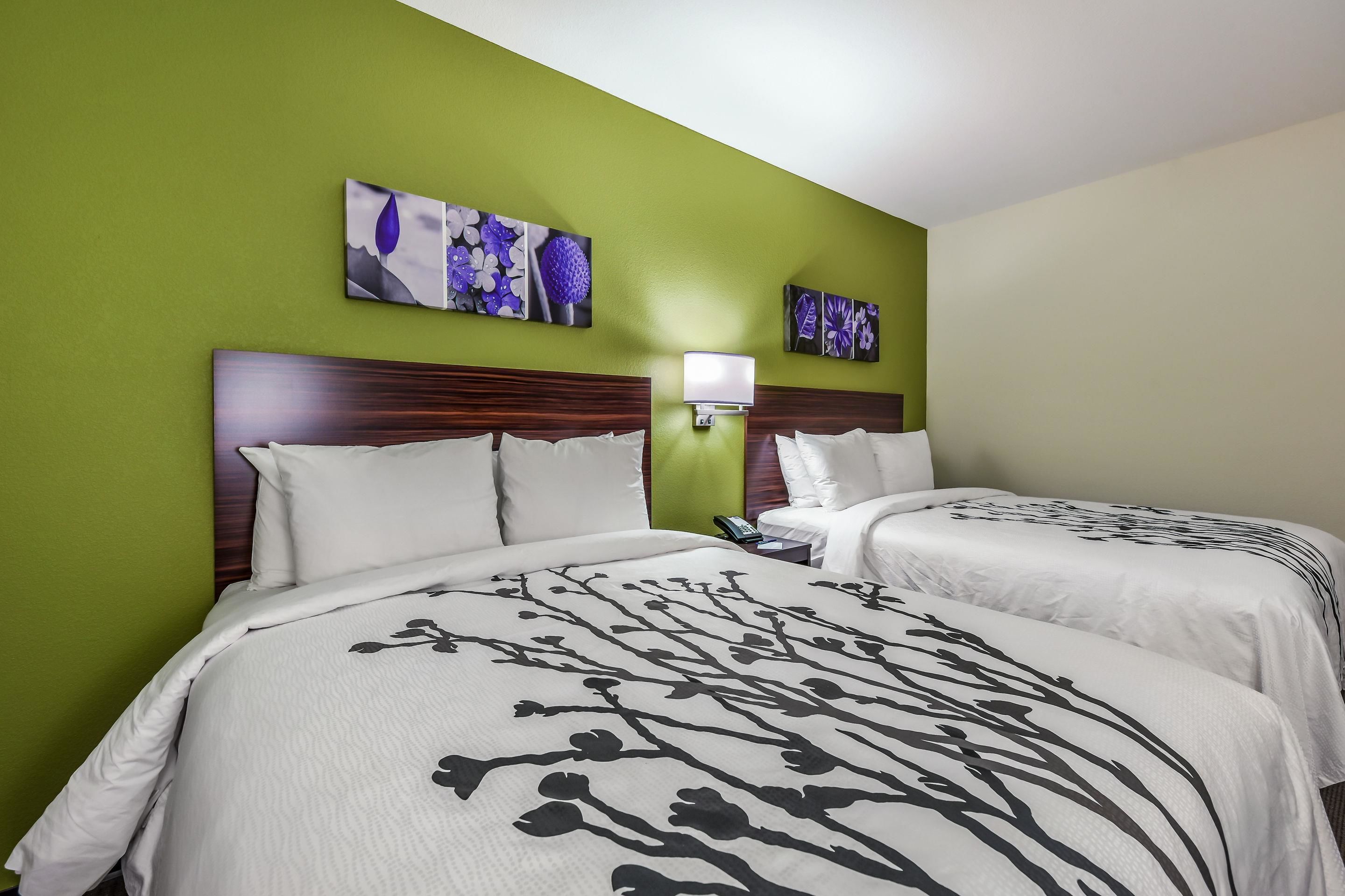 Habitación de hotel con dos camas, paredes verdes y obras de arte con motivos florales.