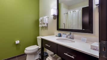 Un baño con un lavabo blanco, tocador de madera oscura, un inodoro blanco y una pared verde.