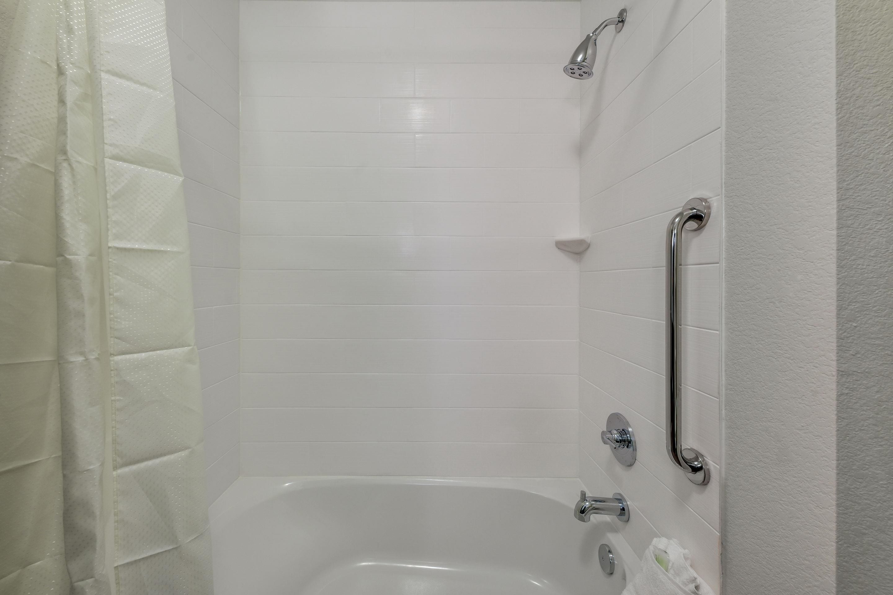 Een badkamer met witte tegels, een badkuip, een douchekop en een handgreep.