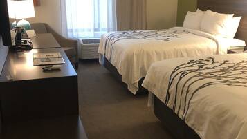 A hotel room with two beds, a desk, a TV, and a window with curtains.