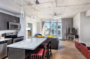 A modern kitchen with a granite countertop, stainless steel appliances, and a dining area with a gray sofa and red chairs.