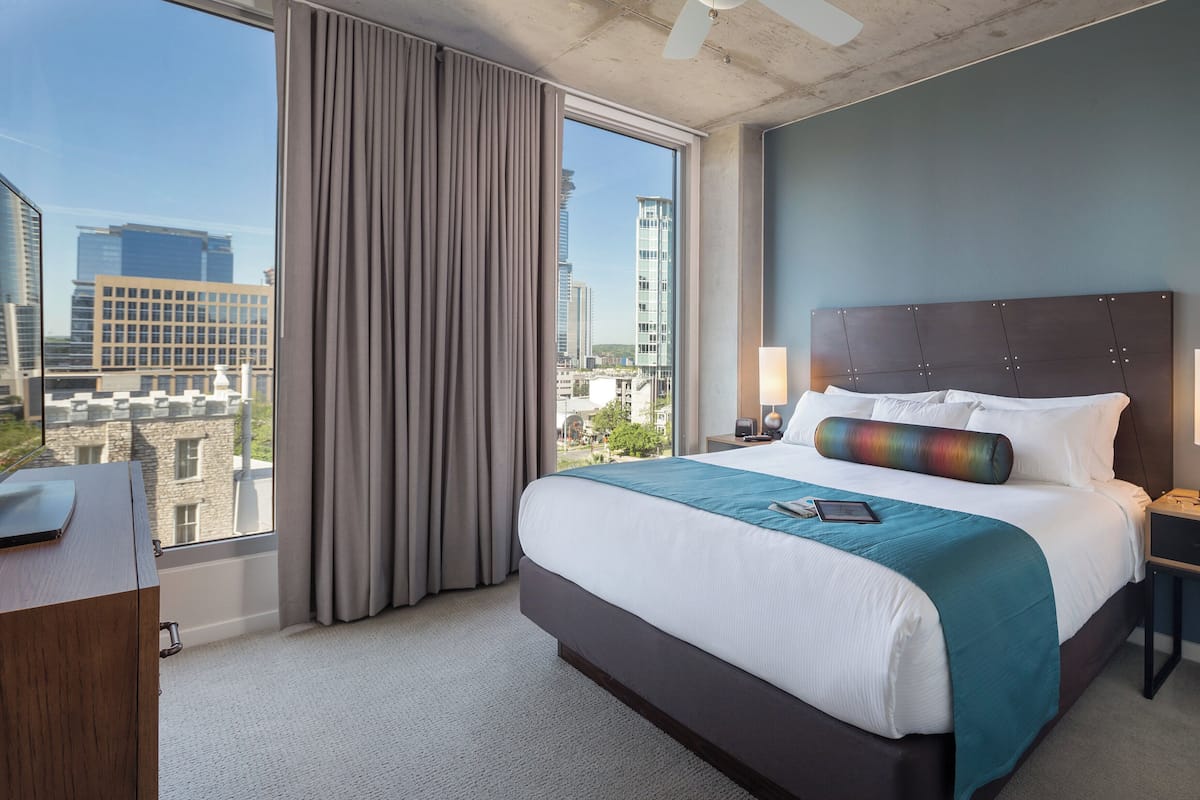 A hotel room with a large bed, a desk, and a view of the cityscape.