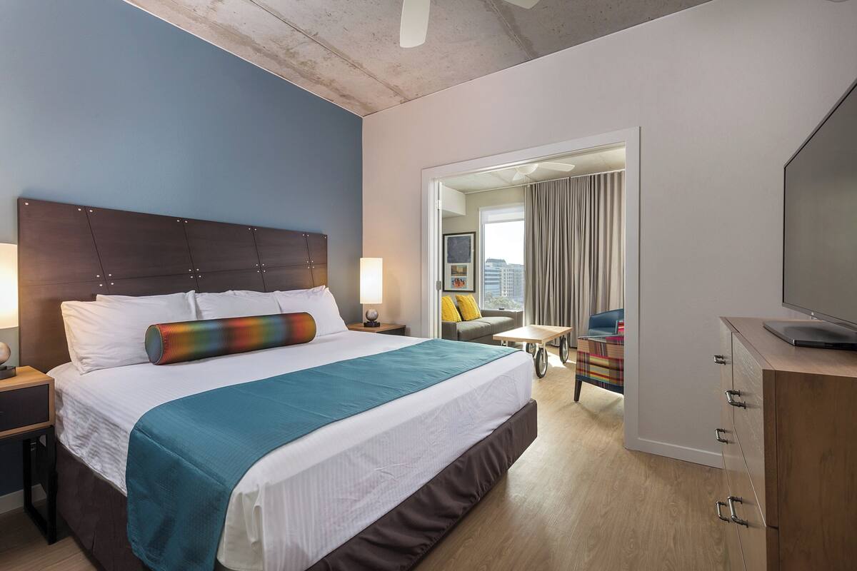 A hotel room with a large bed, a TV, a desk, and a view of the city.