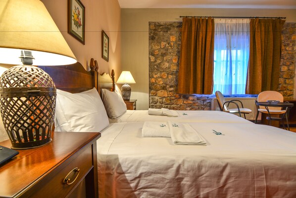 A hotel room with a bed, two bedside tables, a lamp, a chair, a table, and a stone wall. - Karyatis Resort (Xylokastro-Evrostina)