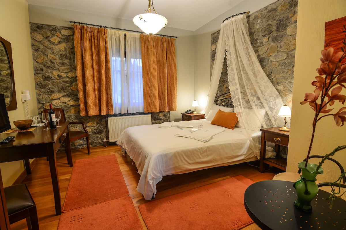 A bedroom with a stone wall, a bed with a canopy, a dining table, and a vase with flowers.