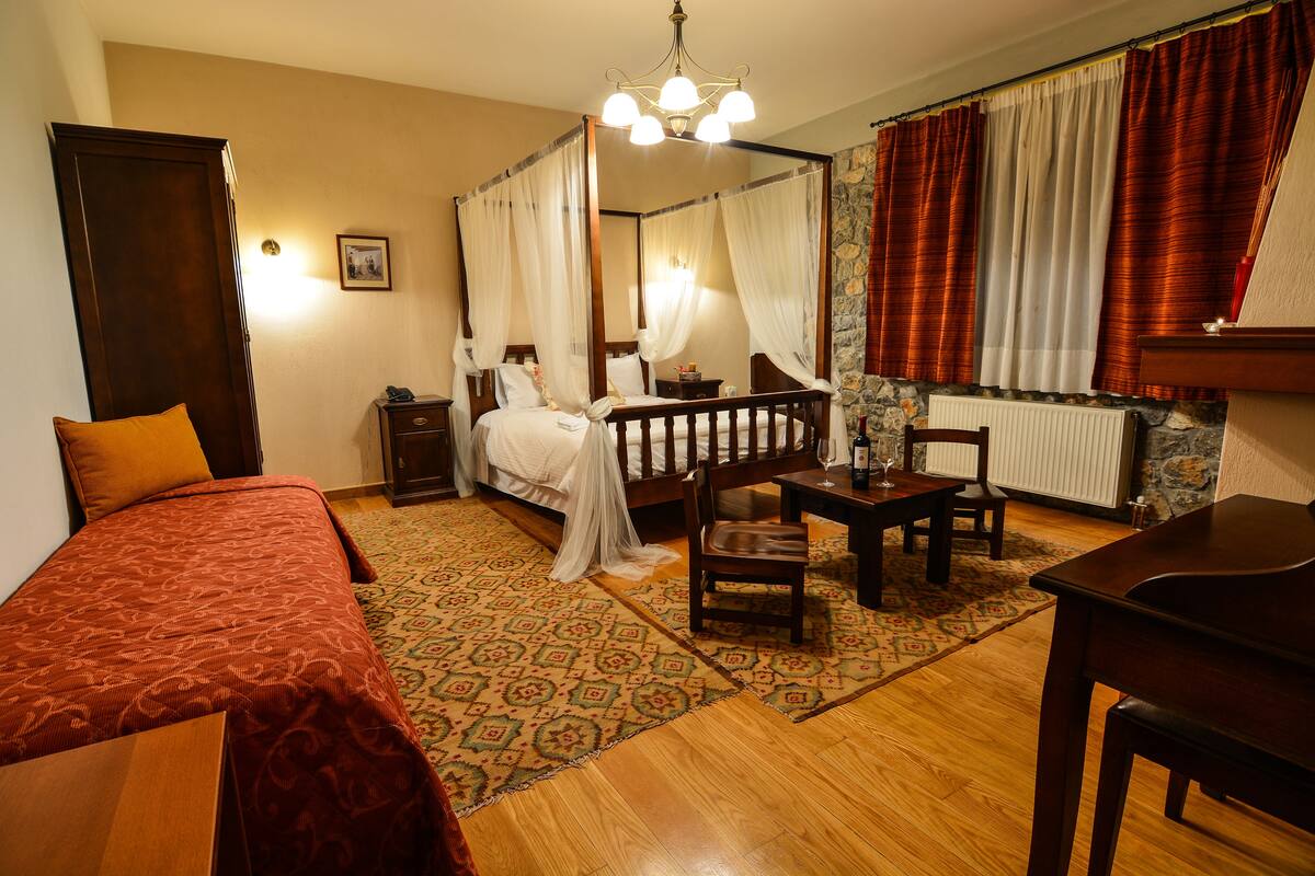 A four-poster bed with a canopy, a wooden desk, a chair, and a small table with a lamp.