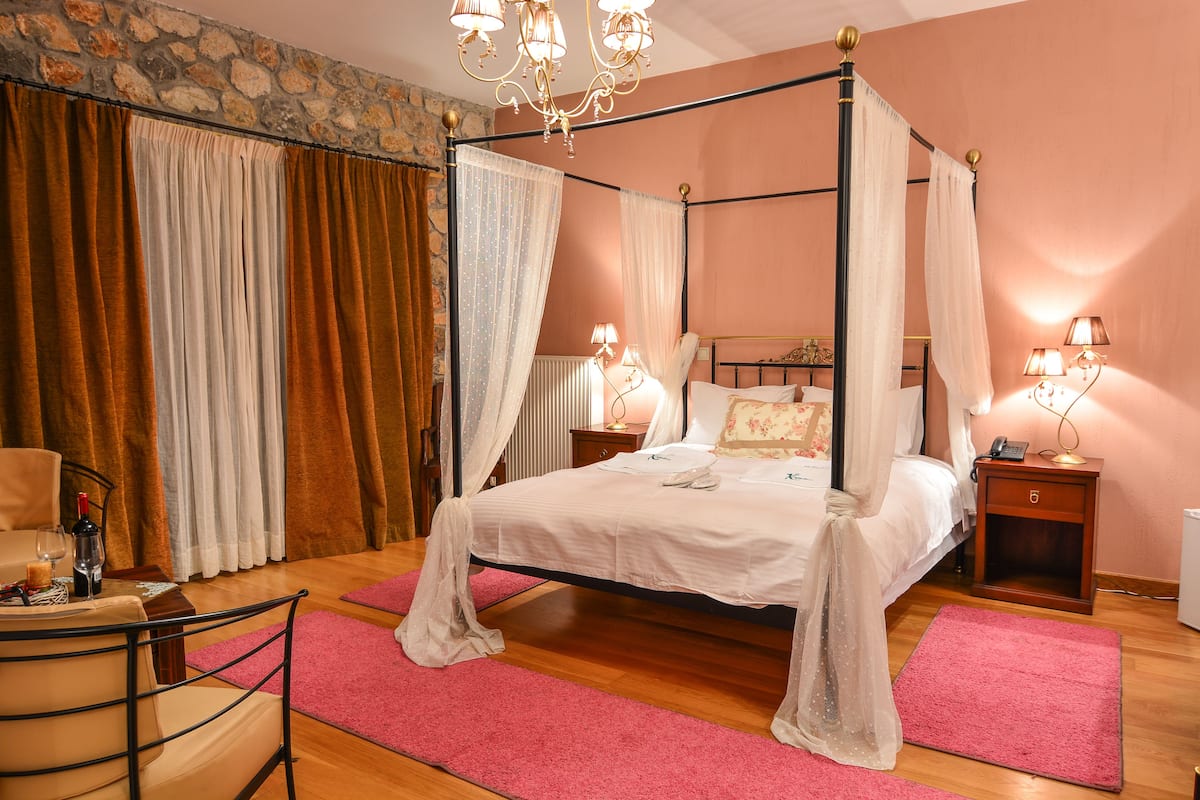 A four-poster bed with a canopy, a wooden nightstand with a lamp, and a chair with a table beside the bed.