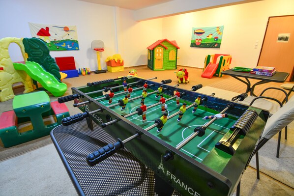 Una habitación con mesa de fútbol, estructuras de juego coloridas y una pequeña maqueta de una casa.