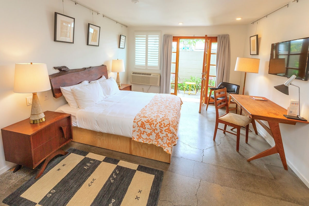 Habitación de hotel con cama, lámparas de noche, escritorio con silla, televisor y vista al exterior.
