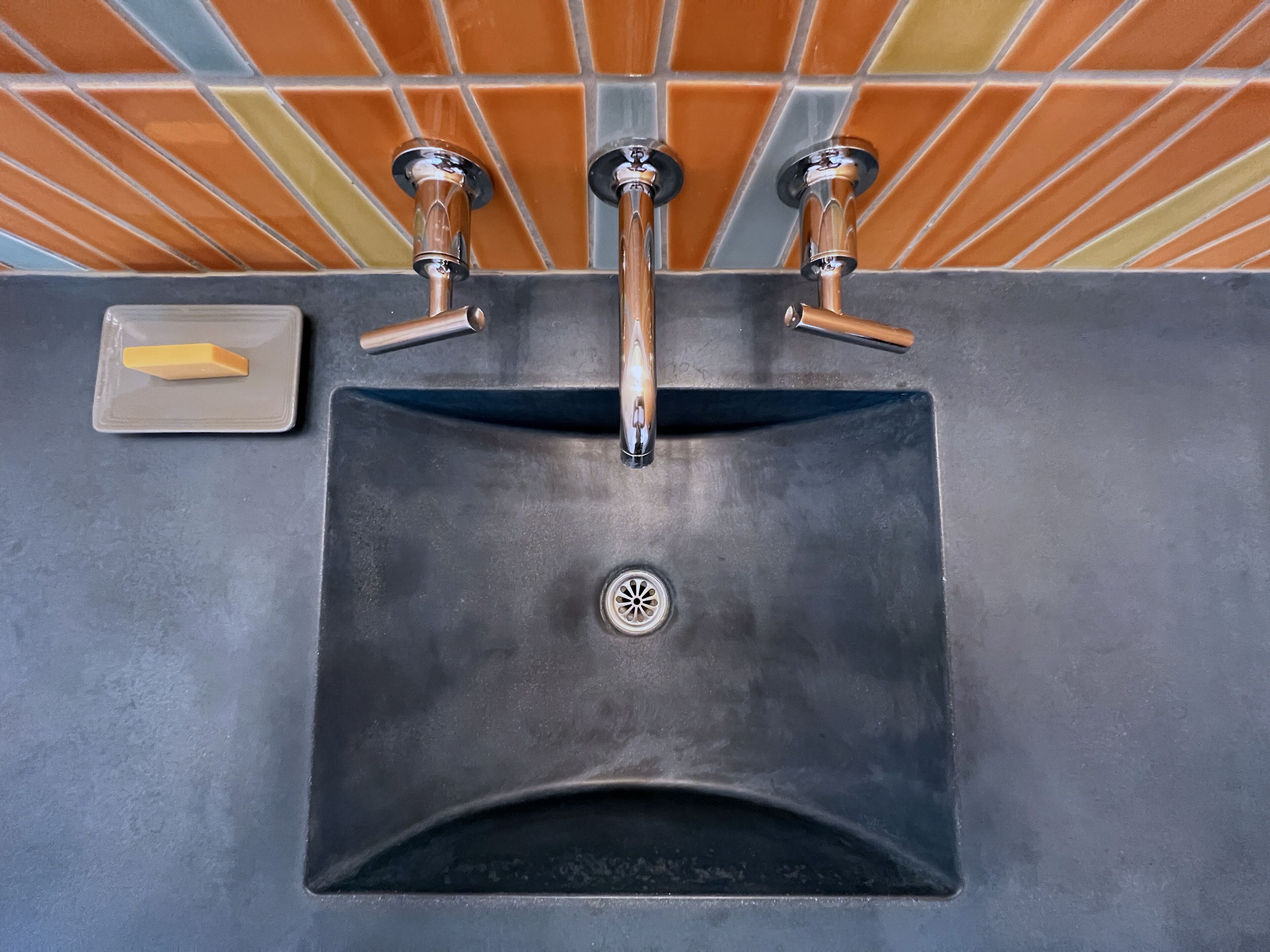 A bathroom sink with a drain, a soap dish, and a tiled backsplash.