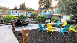A courtyard with colorful Adirondack chairs, a large rock feature, and a building with balconies. - The Astro (Santa Rosa)