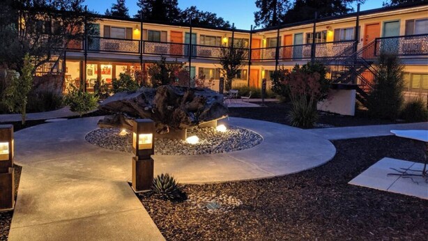 A multi-story hotel with a courtyard featuring a central rock formation and lighting. - The Astro (Santa Rosa)