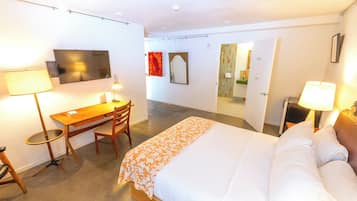 Habitación de hotel con cama, escritorio, silla, televisión y baño visible a través de una puerta abierta.