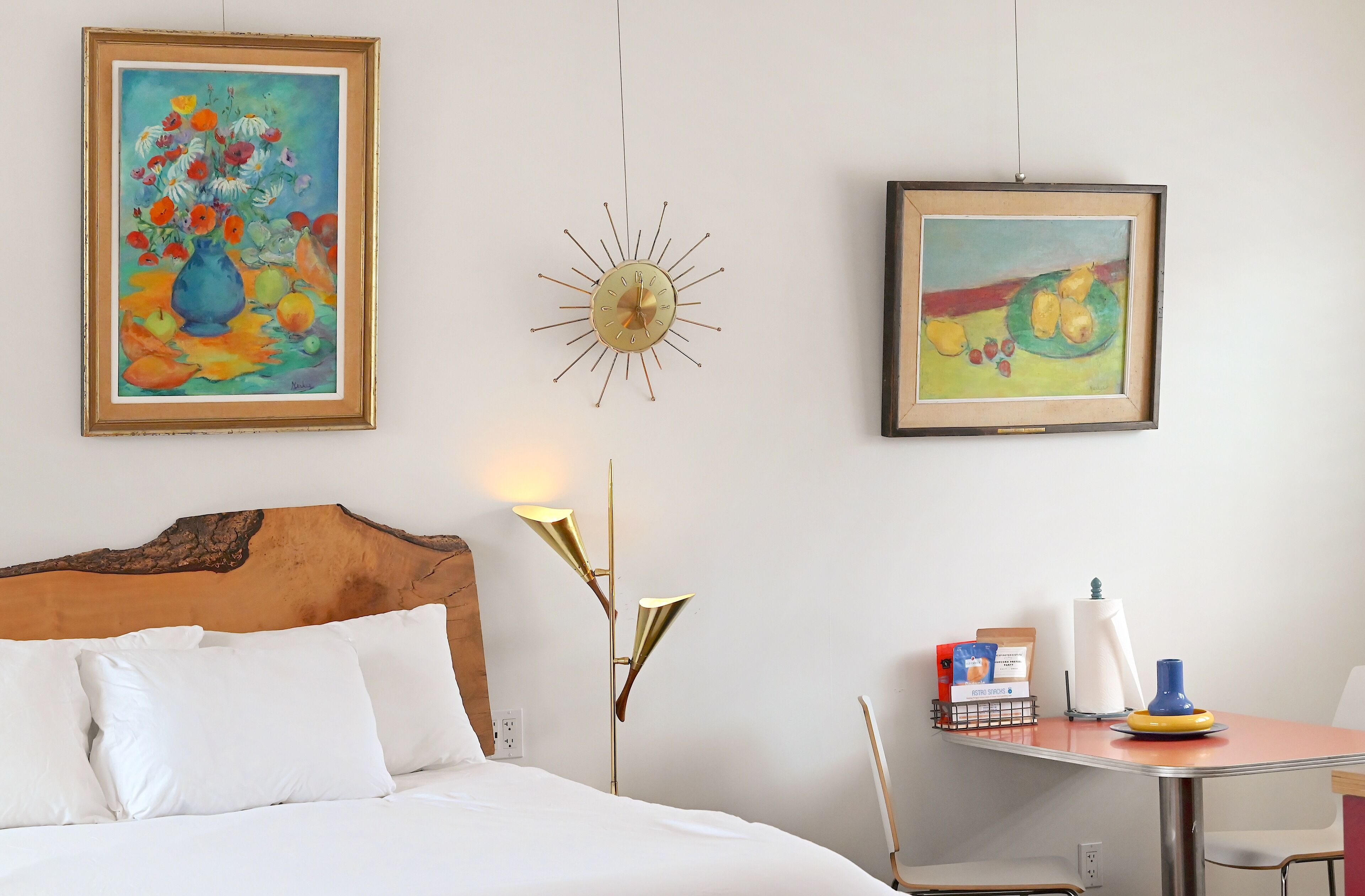 Une chambre d’hôtel avec un lit, un bureau et deux tableaux au mur.