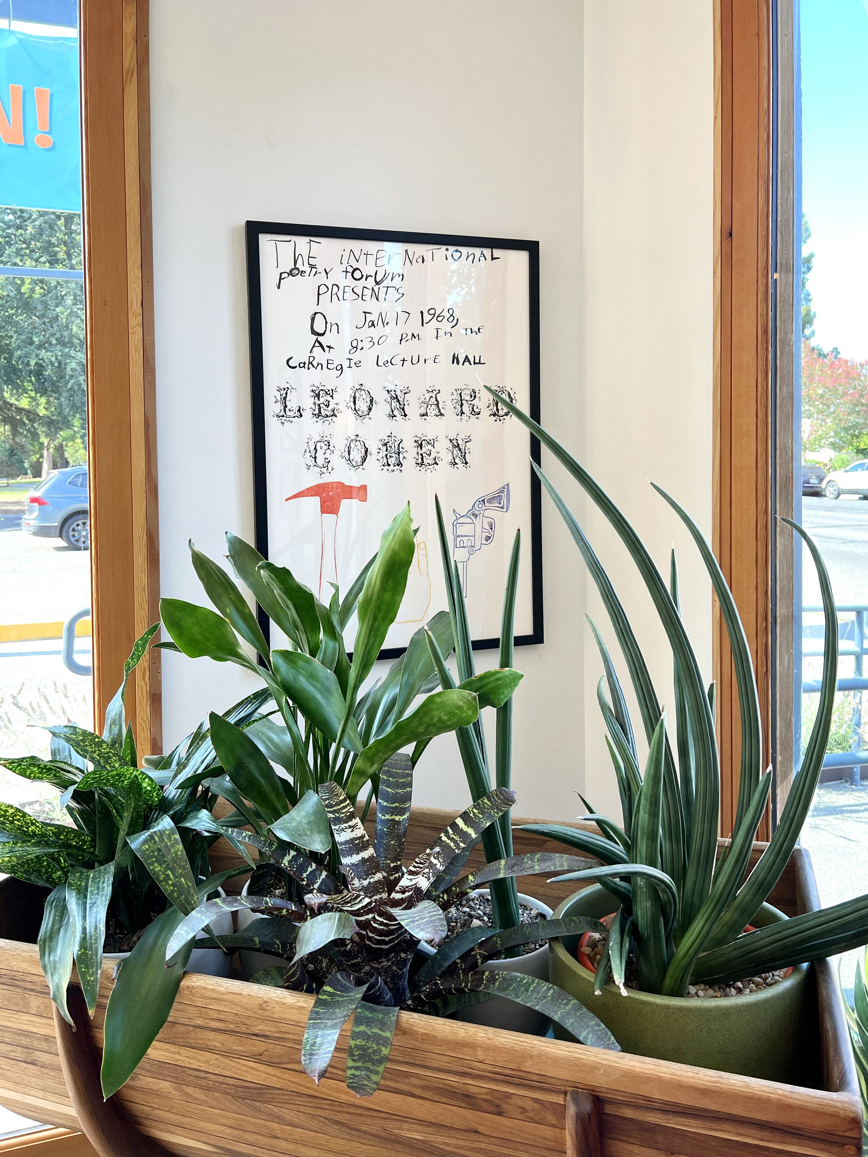 A framed poster on a wall with text and a hammer illustration, surrounded by potted plants.