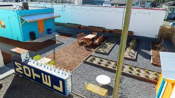 A rooftop patio with a blue building, wooden seating, raised garden beds, and a small table.