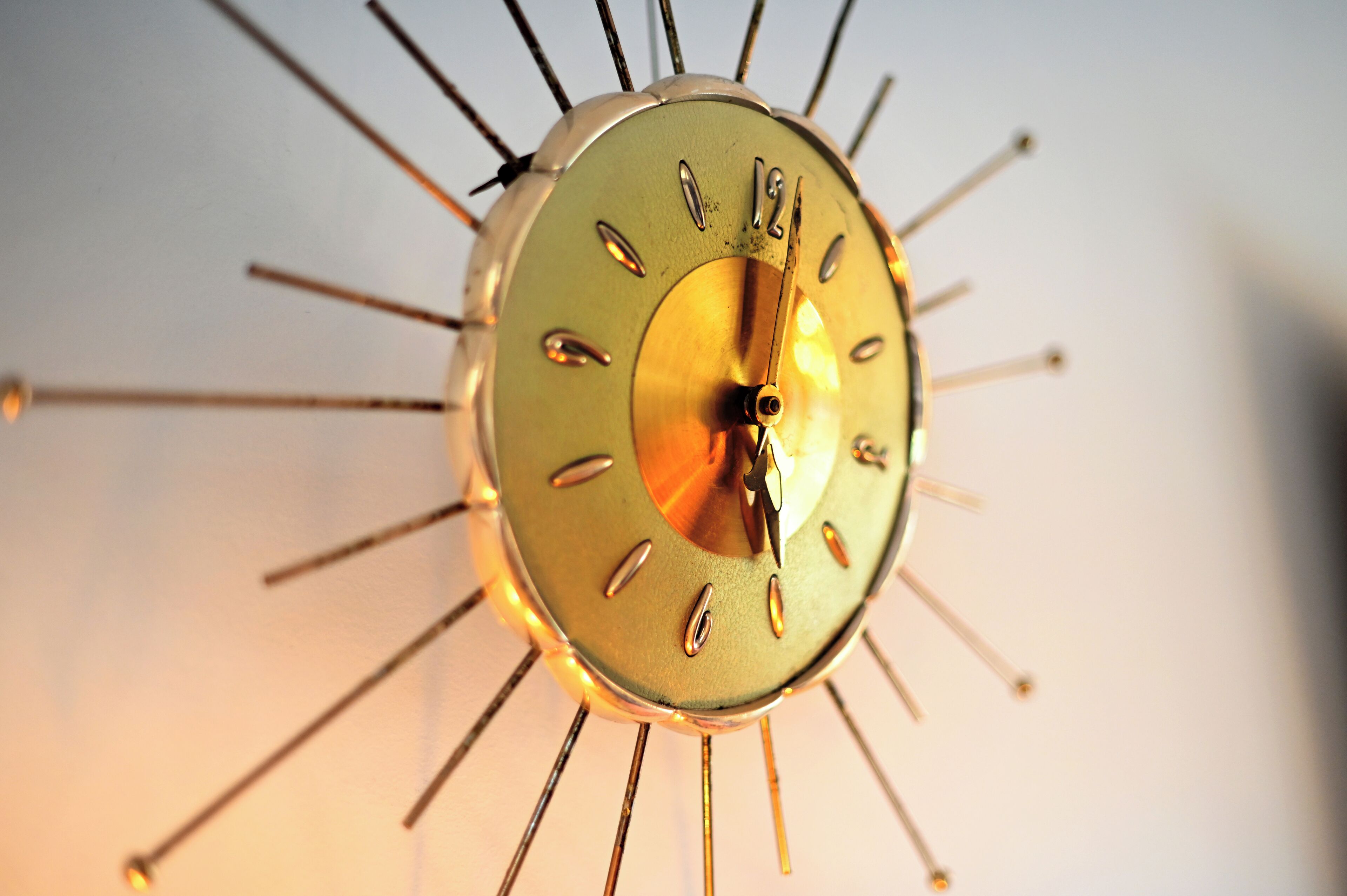 A wall-mounted clock with a sunburst design and a gold finish.