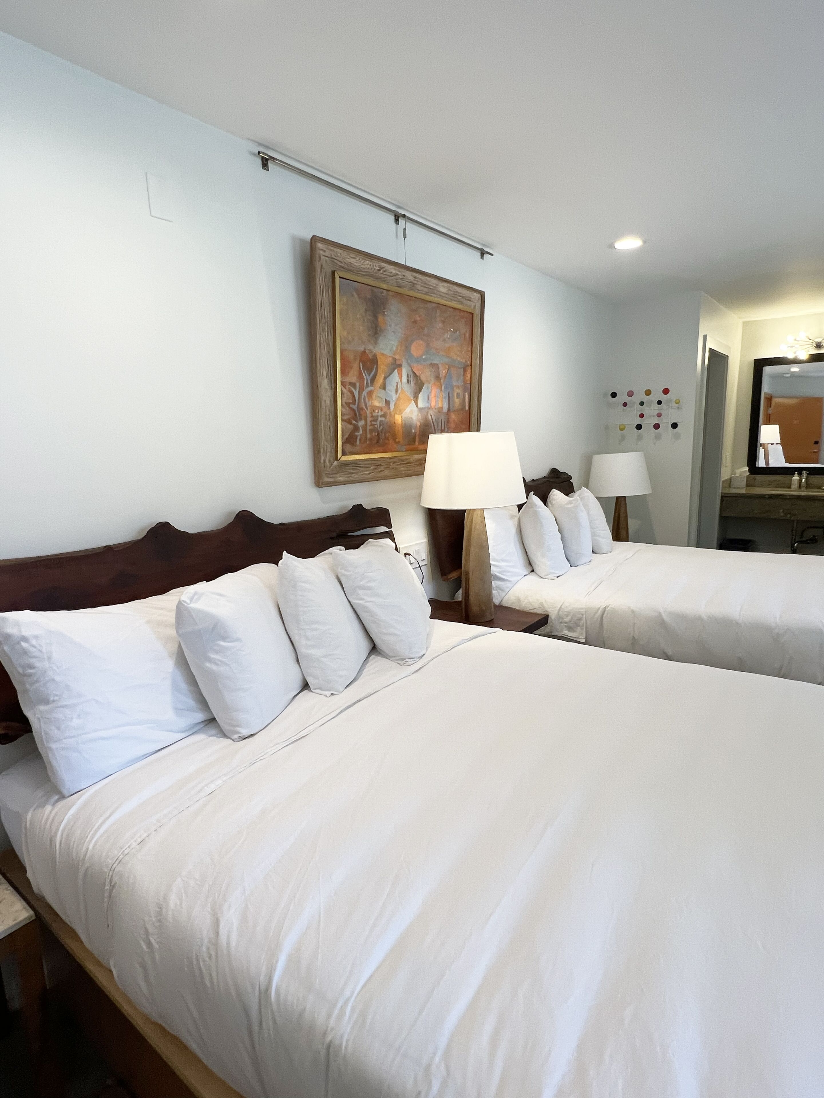 Une chambre d’hôtel avec deux lits, un tableau au mur et un miroir au-dessus du lit.