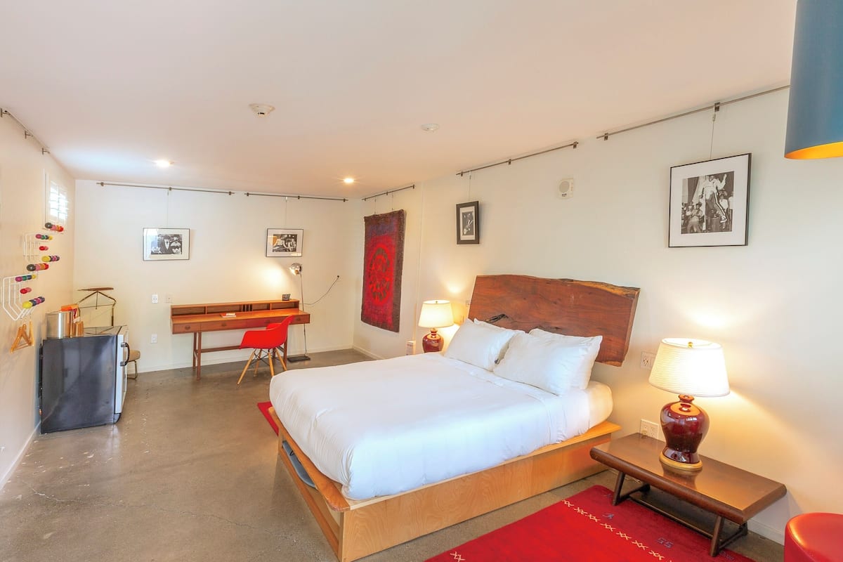 Un dormitorio con cama, escritorio y silla. Hay lámparas de pared y cuadros enmarcados.